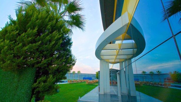 A modern building with a curved glass facade and a well-maintained lawn with palm trees. - Ramada by Wyndham Soma (Soma)