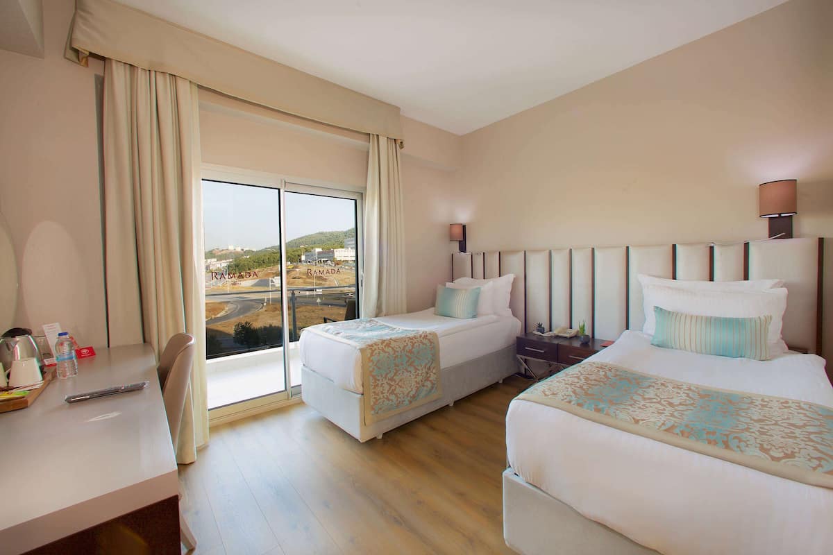 Une chambre d’hôtel avec deux lits, un bureau et une grande fenêtre donnant sur un panorama de la ville.