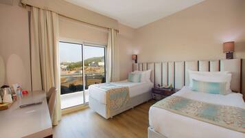 Habitación de hotel con dos camas, un escritorio y un amplio ventanal con vistas a un paisaje urbano.
