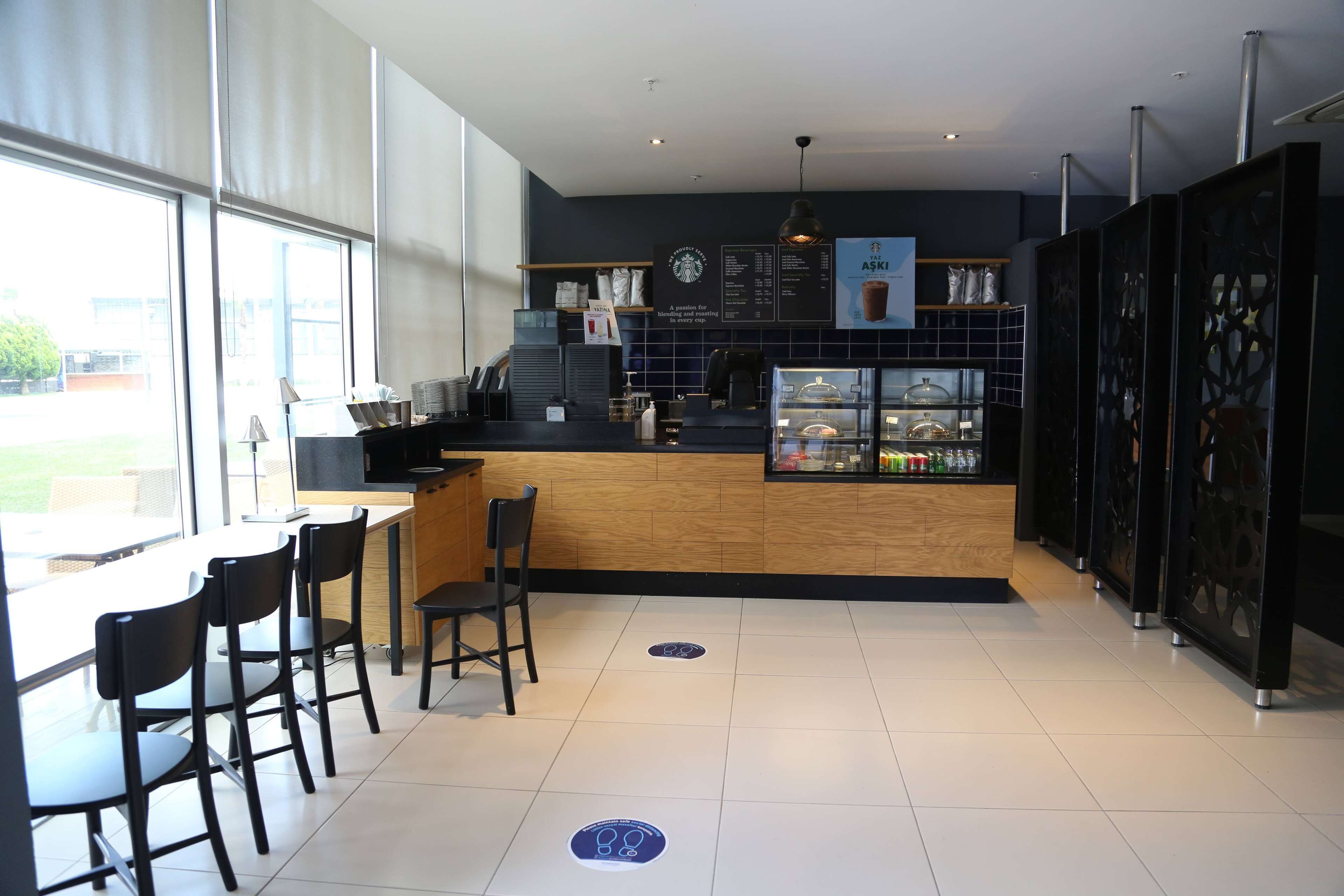 A modern cafe with a wooden counter, black chairs, and a menu board.