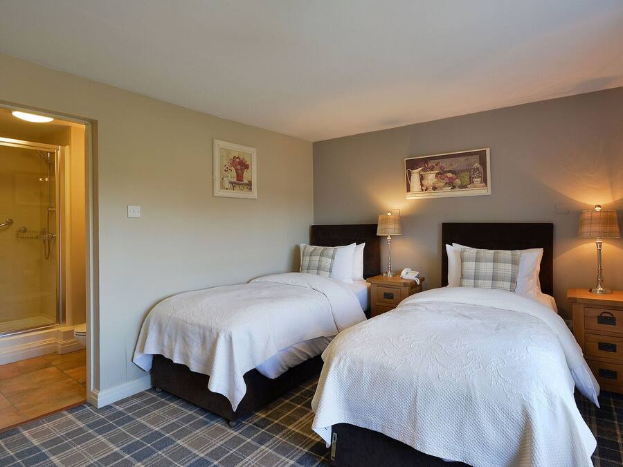 Ein Hotelzimmer mit zwei Betten, einer Dusche und einem kleinen Nachttisch mit Lampe.