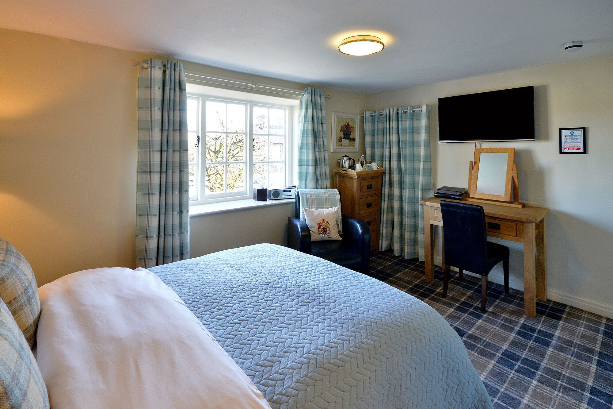 A hotel room with a bed, a desk, a chair, a television, and a window with curtains.