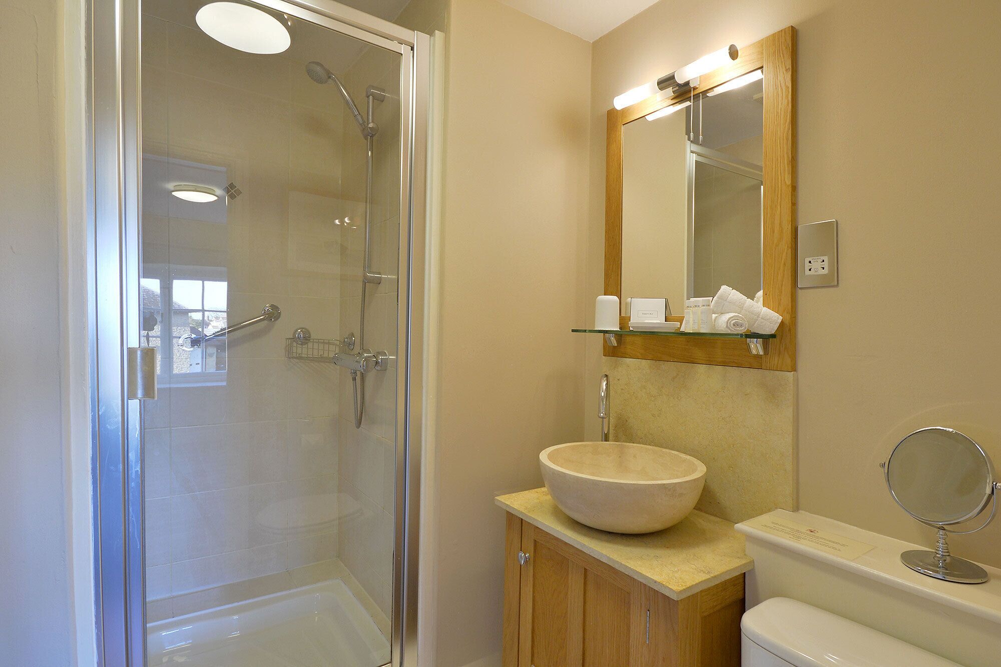 Une salle de bain moderne avec une douche à parois de verre, un meuble-lavabo en bois doté d’un grand lavabo en cuve et un miroir au-dessus du lavabo.