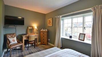 A bedroom with a bed, a desk, a chair, a television, and a window with curtains.