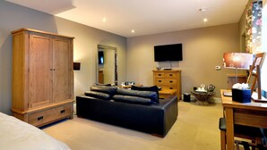 Un dormitorio con un armario de madera, un sofá de cuero negro, un televisor de pantalla plana, un aparador de madera y una lámpara.
