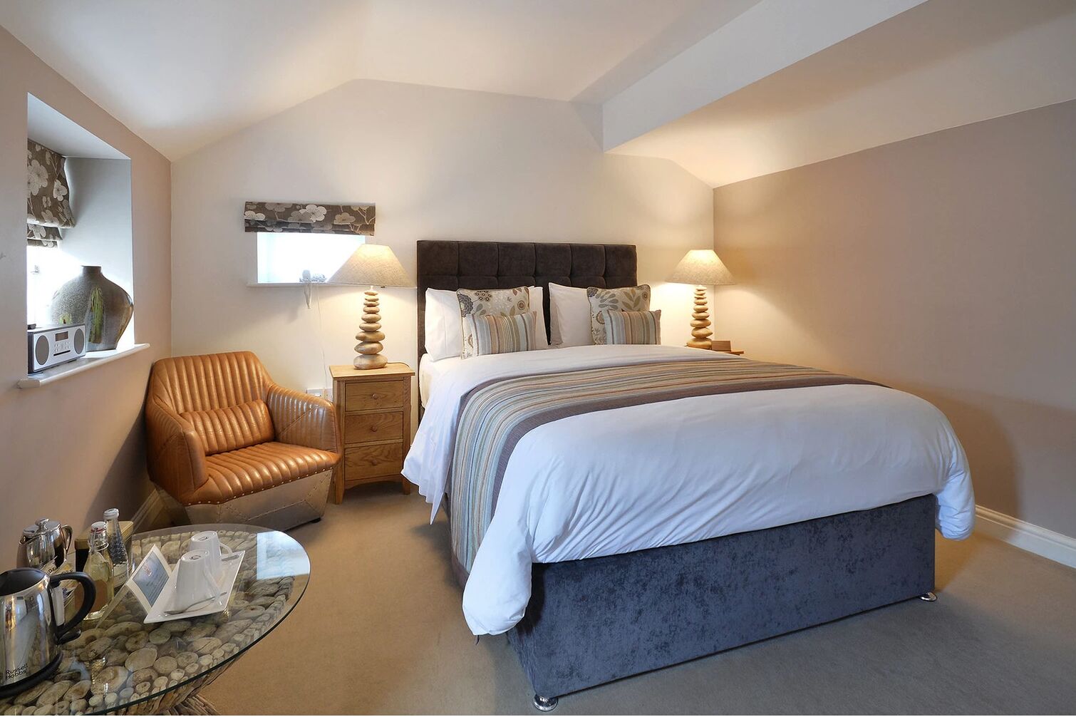 A bedroom with a bed, a chair, a bedside table, and a lamp.