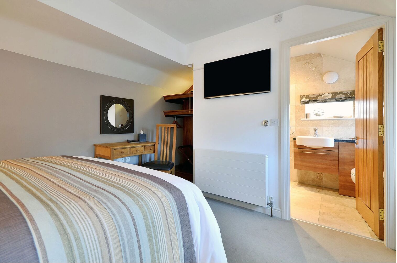 Un dormitorio con cama, escritorio, silla, televisión y baño visible a través de una puerta abierta.