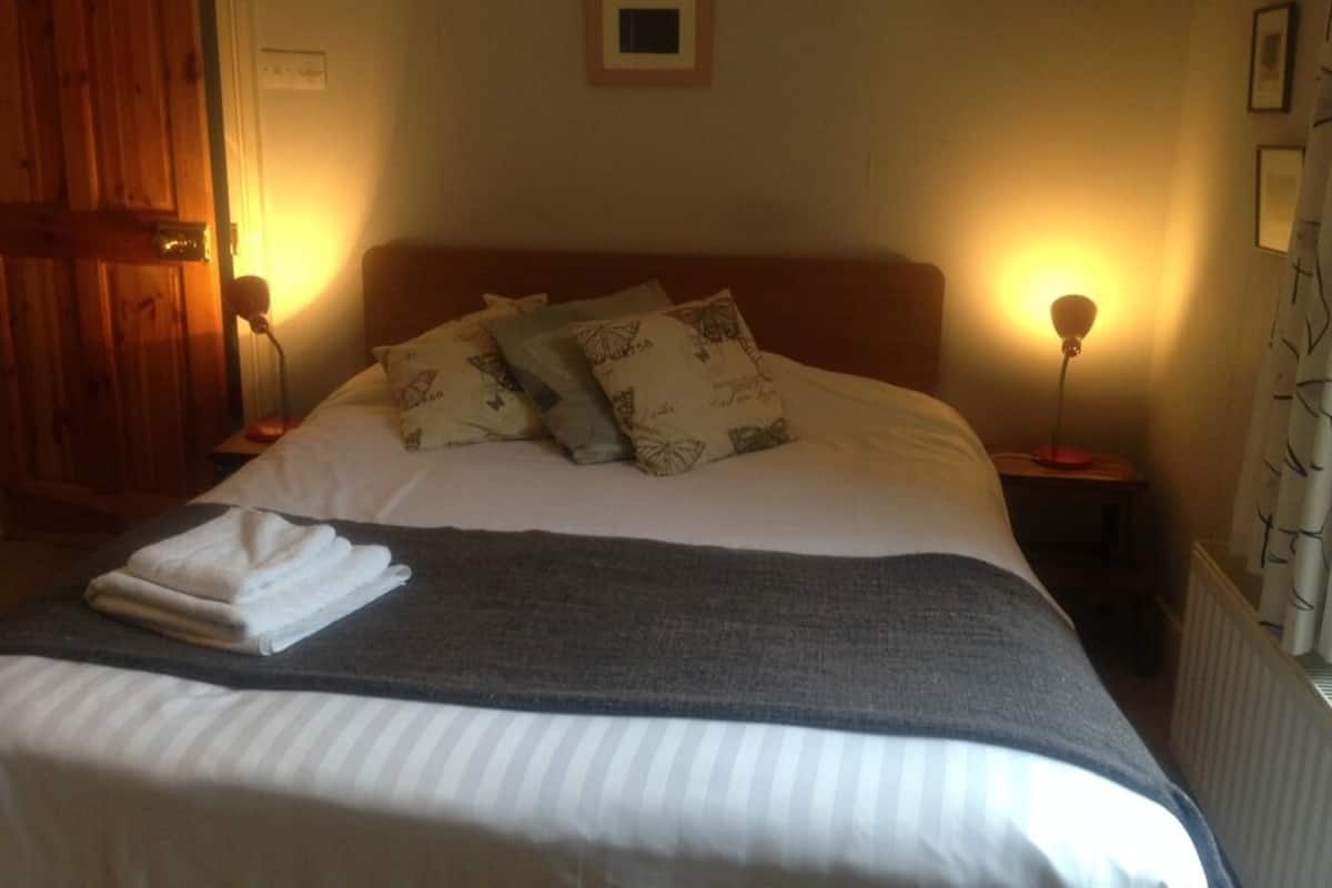 A neatly made bed with a gray blanket and white pillows, two bedside lamps, a framed picture on the wall, and a wooden door.