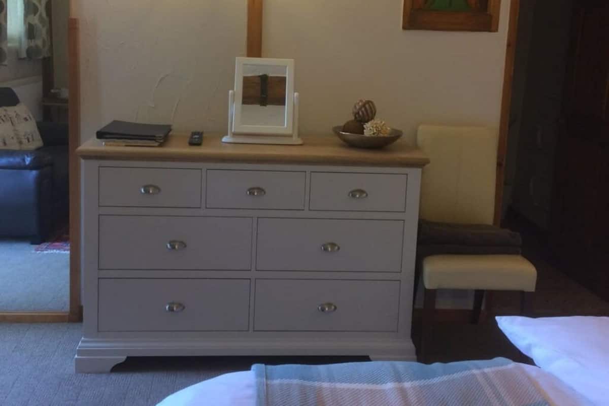 A bedroom with a bed, a dresser with drawers, a bedside table, and a chair.