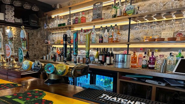 Eine Bar mit mehreren Zapfhähnen, einem Computer und einer Tastatur mit der Aufschrift 'THATCHERS'.