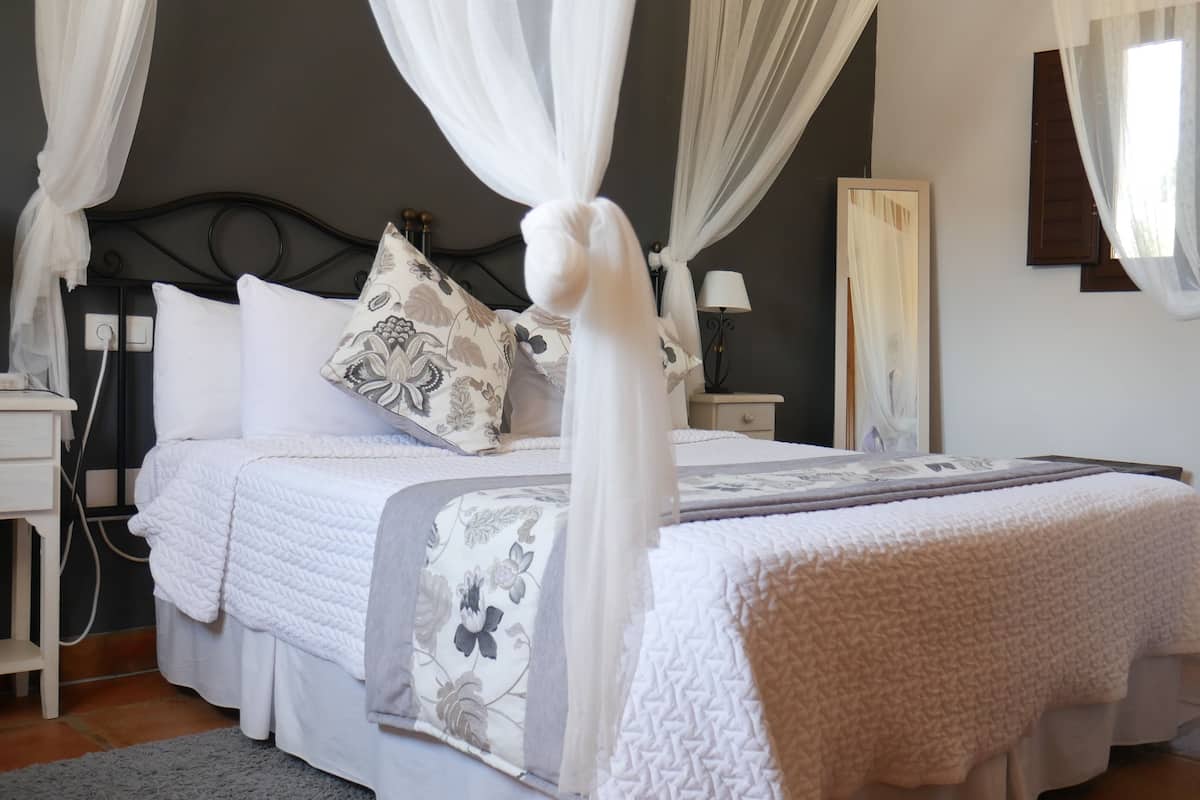 A bedroom with a four-poster bed, a nightstand, a lamp, and a painting on the wall.