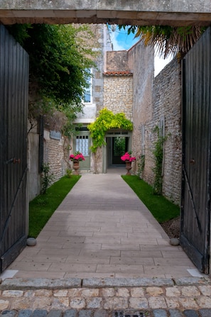 Un étroit sentier de pierre menant à une porte, bordé de verdure et de plantes en pot.