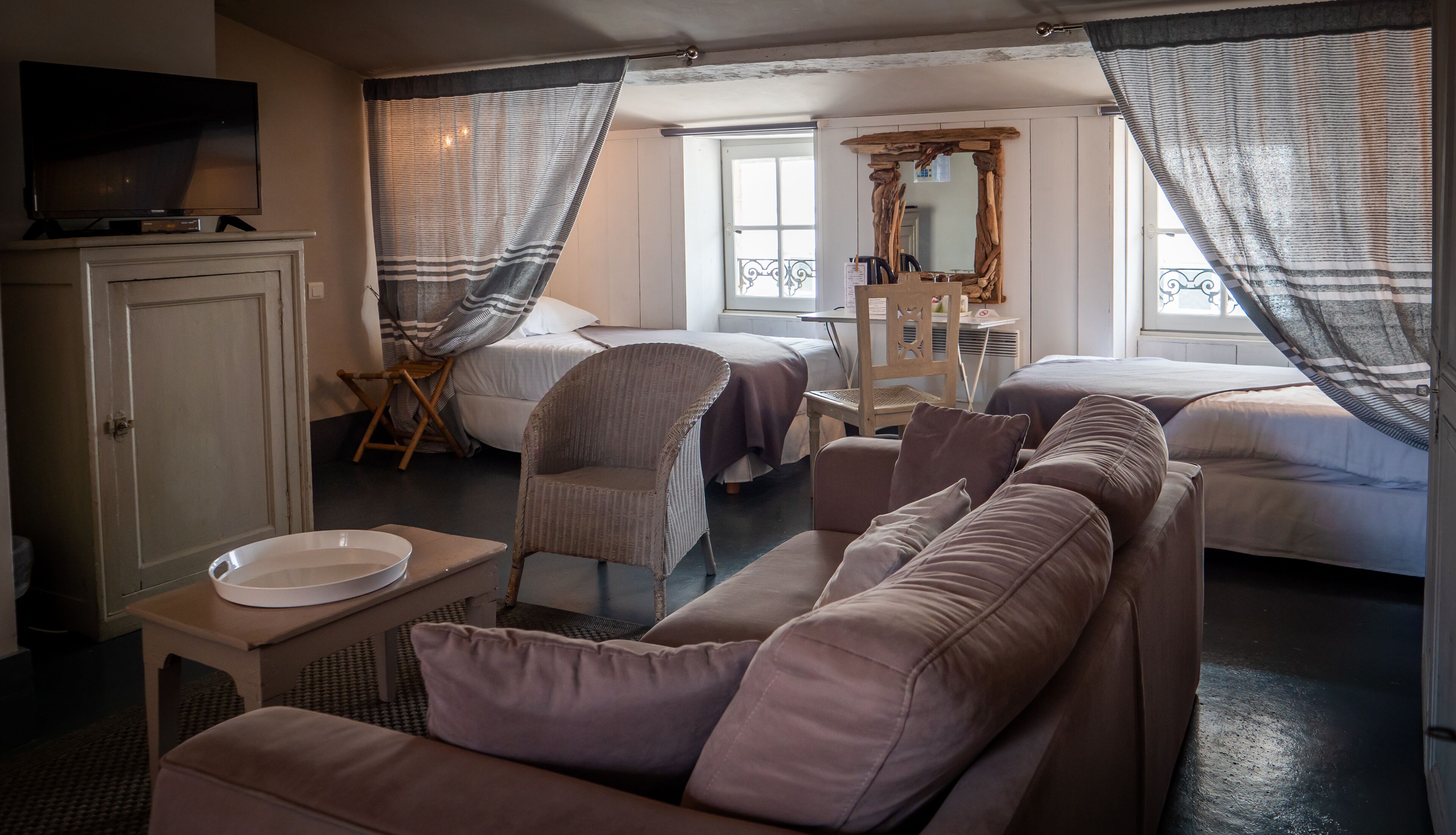 A hotel room with two beds, a sofa, a television, a mirror, and a small table with a bowl.