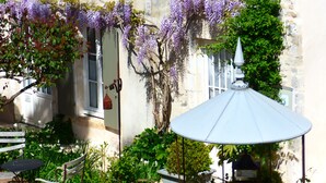 A courtyard with a white table and bench, surrounded by lush greenery and purple flowering vines. - La Maison Douce (Saint-Martin-de-Re)