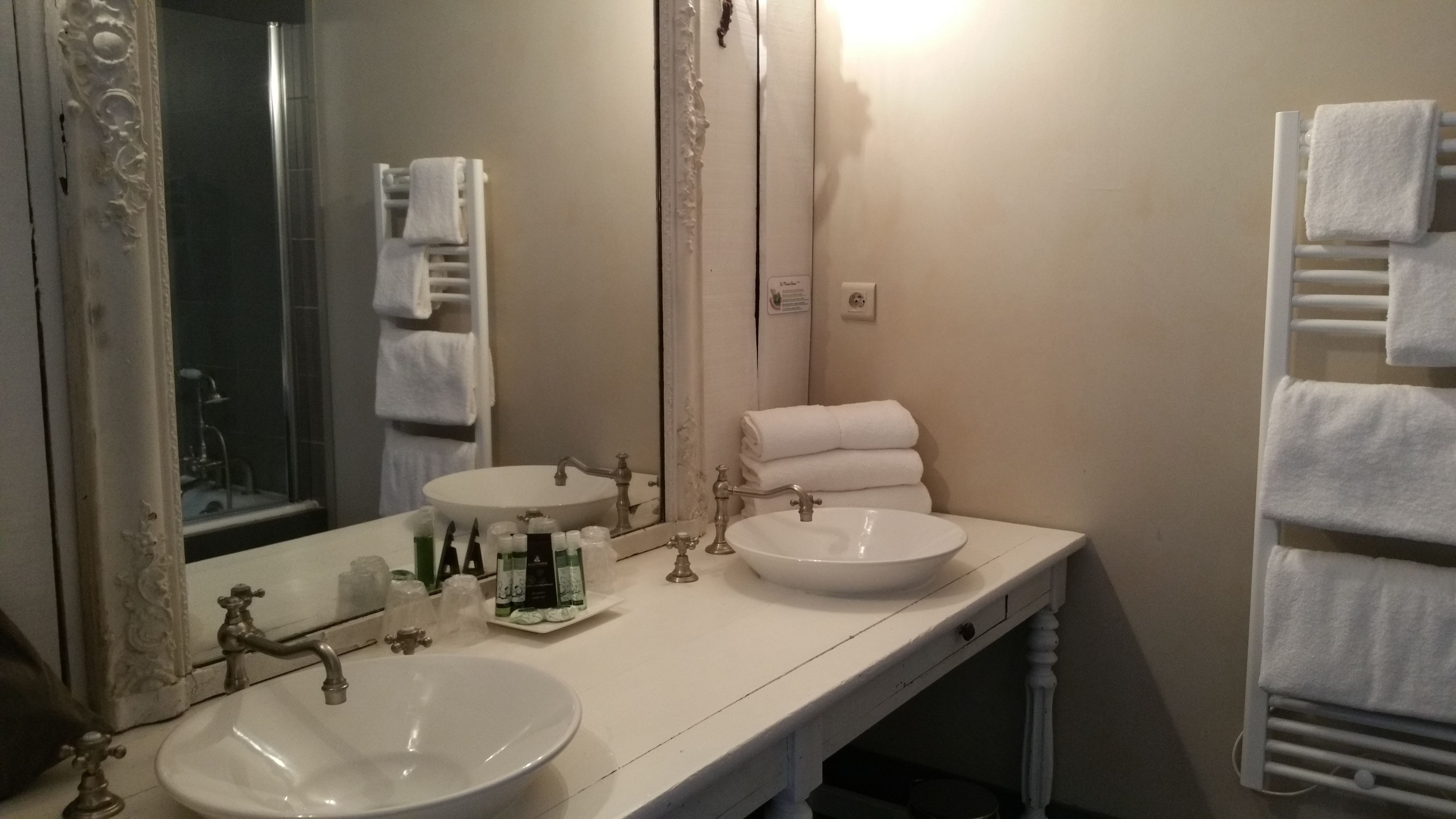 A bathroom with two sinks, a large mirror, and a towel rack with multiple towels.