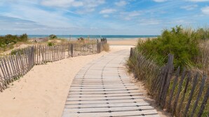 A wooden boardwalk leading to a sandy beach with a wooden fence on one side and vegetation on the other. - La Maison Douce (Saint-Martin-de-Re)