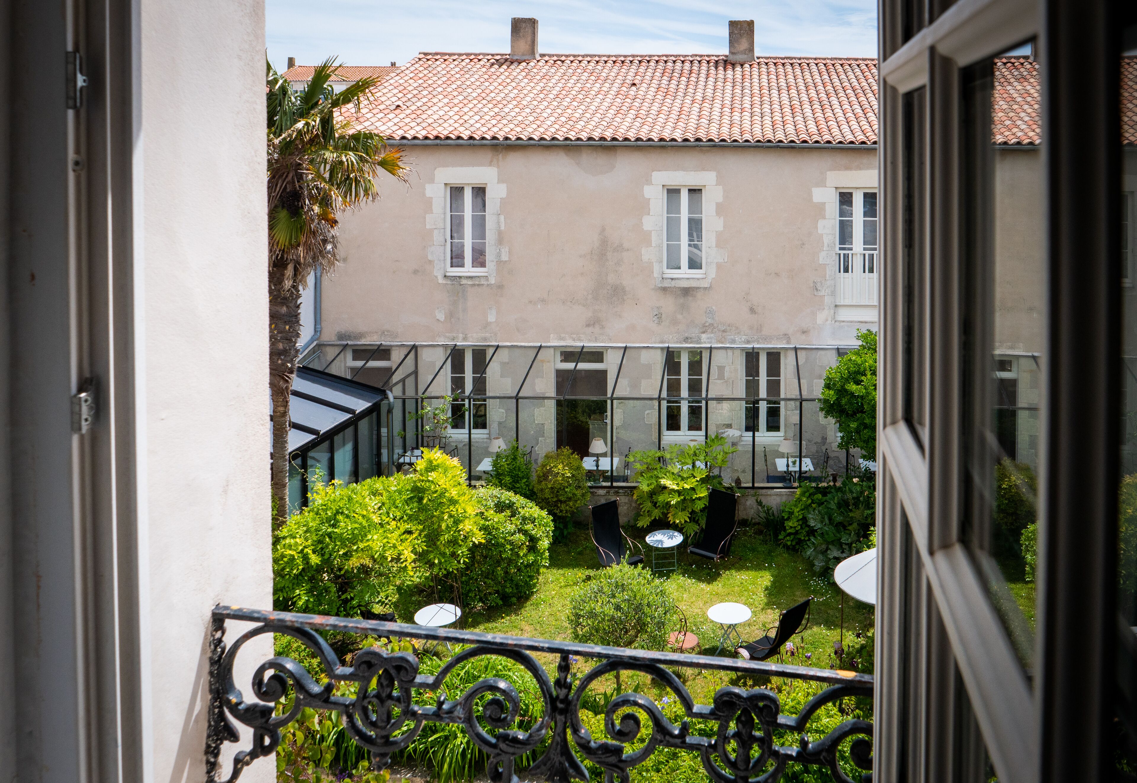Une cour donnant sur un bâtiment doté d’un toit en tuiles et d’un balcon orné d’une balustrade en fer forgé.