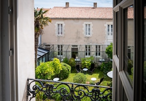 A courtyard with a view of a building with a tiled roof and a balcony with a wrought iron railing. - La Maison Douce (Saint-Martin-de-Re)