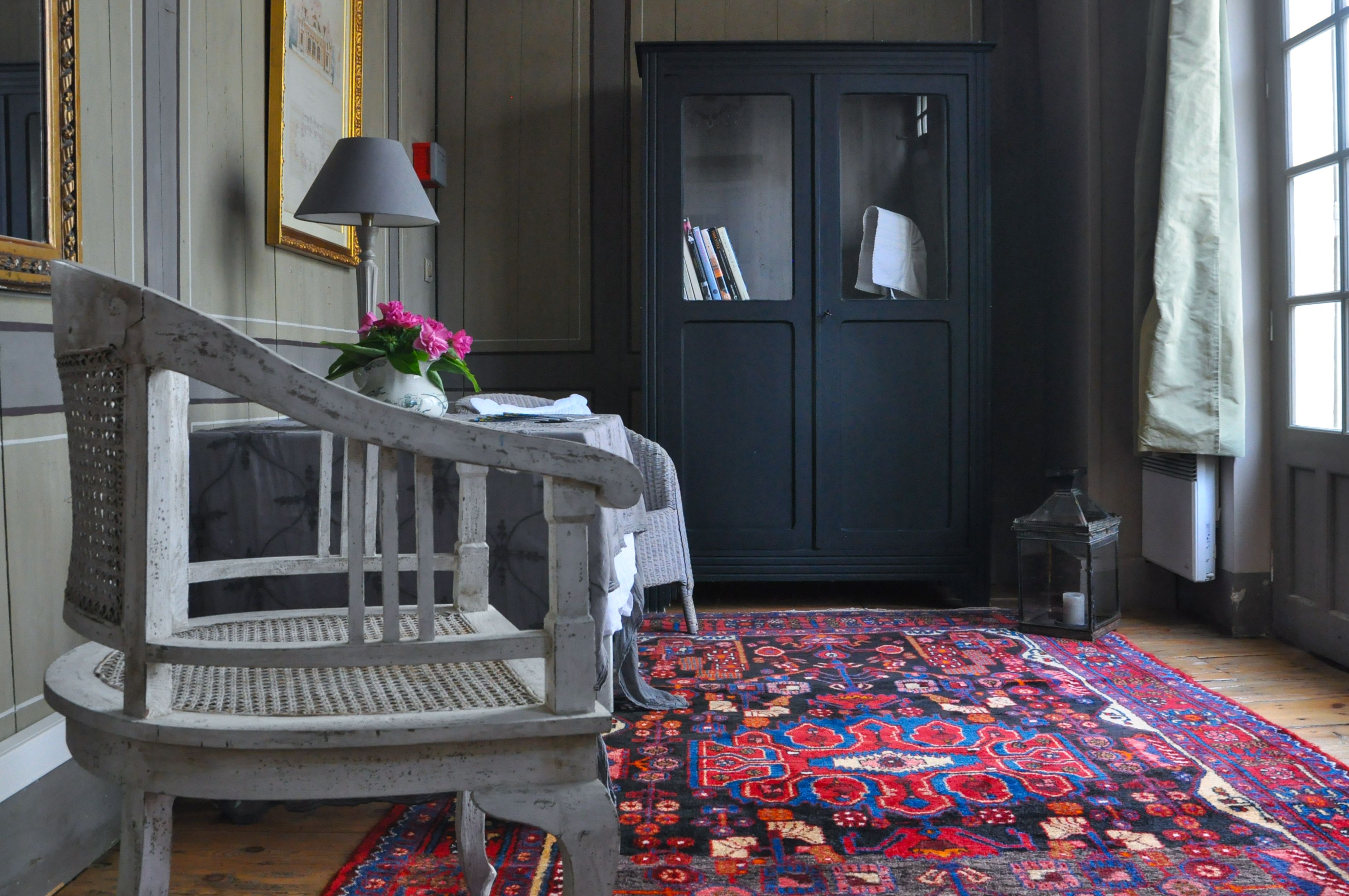 A room with a patterned rug, a chair, a dark cabinet with books, and a lamp.