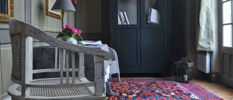 A room with a patterned rug, a chair, a dark cabinet with books, and a lamp.