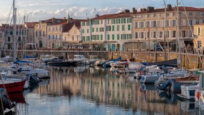 A marina with various boats docked, buildings with green shutters, and a calm water surface reflecting the surroundings. - La Maison Douce (Saint-Martin-de-Re)