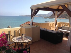 A terrace with a table and chairs, overlooking a coastal view with a mountain in the distance.