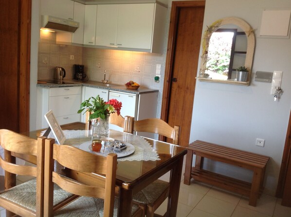 A dining area with a wooden table, chairs, and a bench. There is a vase with flowers on the table. - Asterias Studios Apartments (Apokoronas)