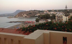 A coastal town with buildings on a hillside, a beach with umbrellas, and a mountain in the background. - Asterias Studios Apartments (Apokoronas)