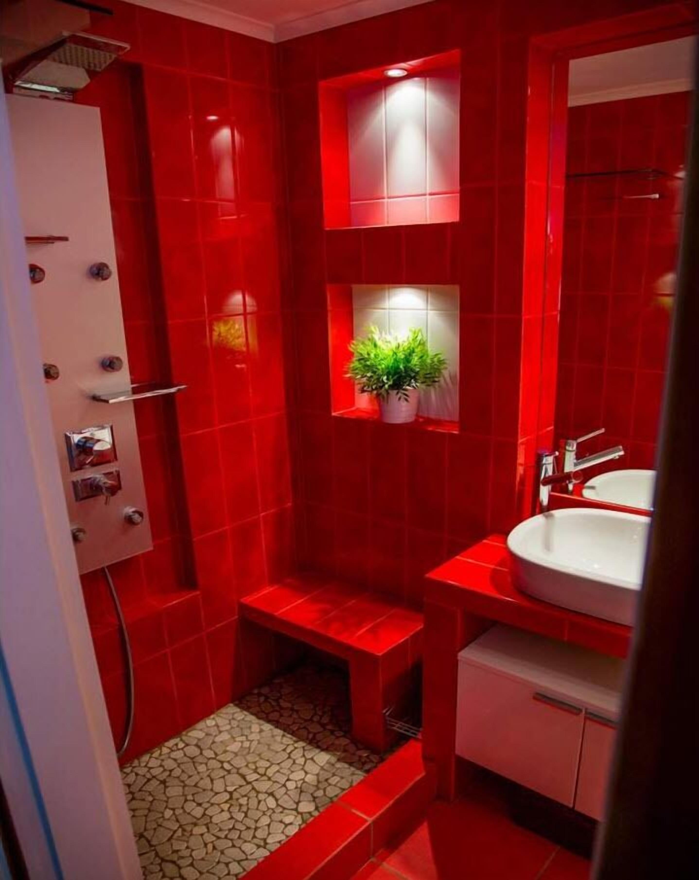 A bathroom with red tiles, a white sink, a small window with a plant, and a shower area.