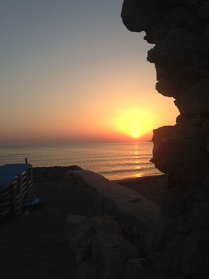 A sunset over the ocean with a rocky cliff and a beach area.
