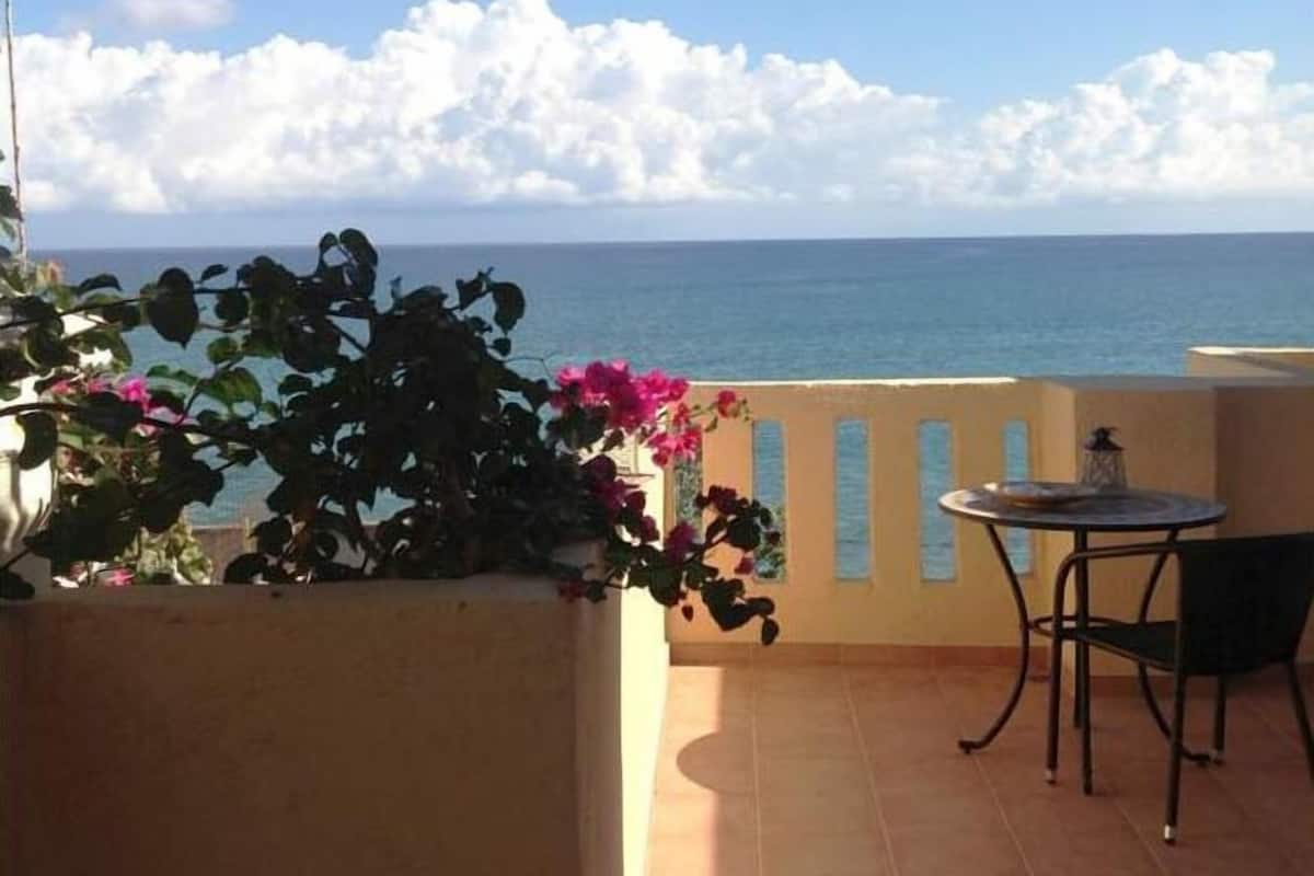 Un balcón con vista al mar, una mesa y sillas.