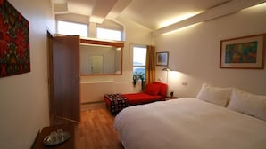 A hotel room with a bed, a red chair, a small table, a mirror, and a painting on the wall. - Lónkot Rural Resort (Skagafjörour)