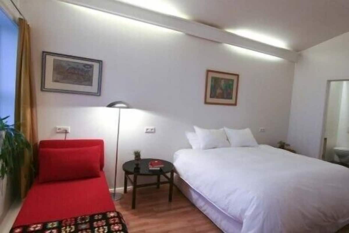 A hotel room with a bed, a red sofa, a small table, and a painting on the wall.