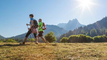 Two hikers walking on a grassy field with a mountainous backdrop and a clear sky.