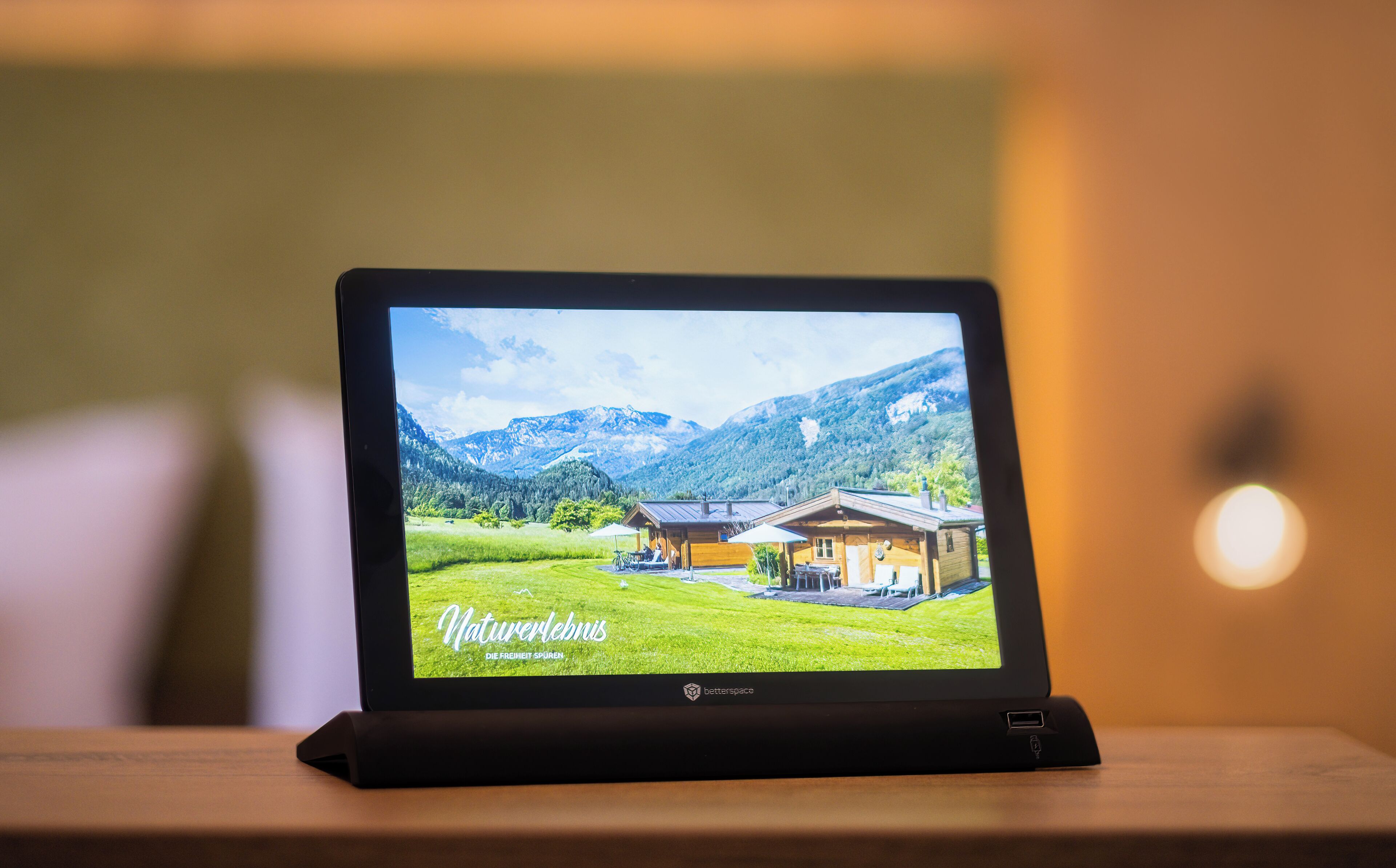 Ein Tablet zeigt eine malerische Landschaft mit einer Holzhütte, Bergen und dem Schriftzug 'Naturerlebnis' auf dem Bildschirm.