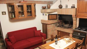 A kitchen with a brick oven, a red sofa, wooden cabinets, and a dining table with chairs. - Il Focolare (Todi)