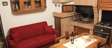 Una cocina con horno de ladrillo, un sofá rojo, armarios de madera y una mesa de comedor con sillas.