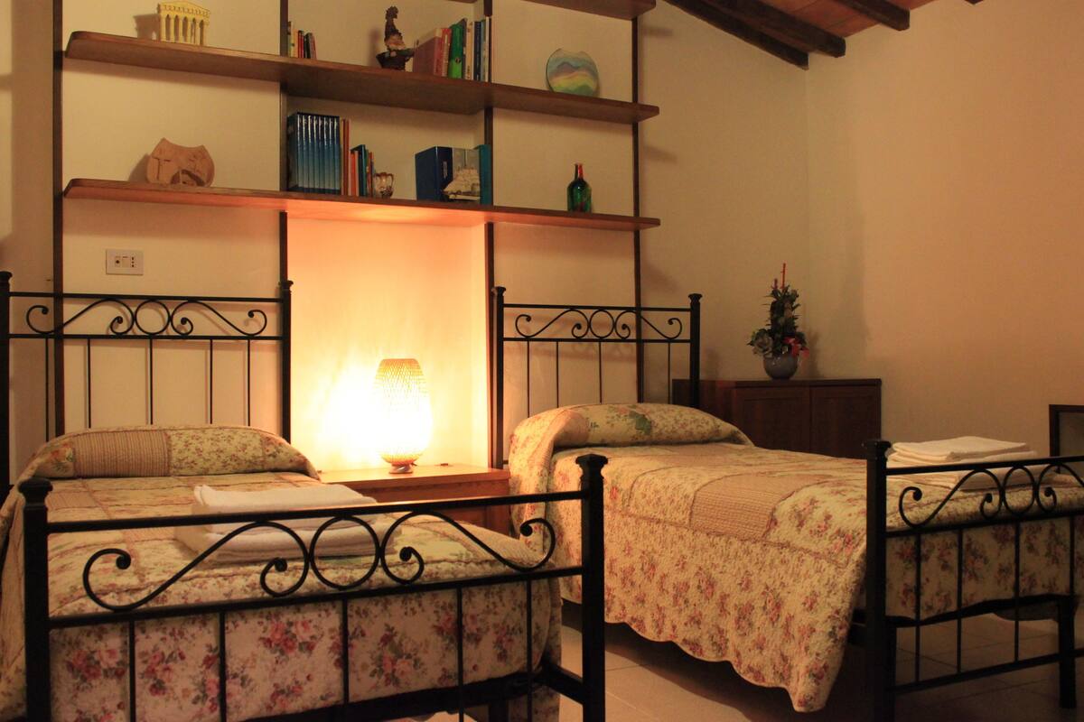 Una habitación con dos camas, una estantería con libros y objetos decorativos, y un pequeño árbol de Navidad.