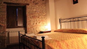 A bedroom with a stone wall, a wooden door, a metal bed frame, and a bedside table with a lamp. - Il Focolare (Todi)