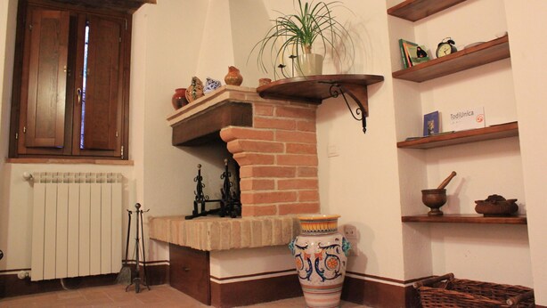 A traditional room with a brick fireplace, a large decorative vase, and wooden shelves with various items. - Il Focolare (Todi)