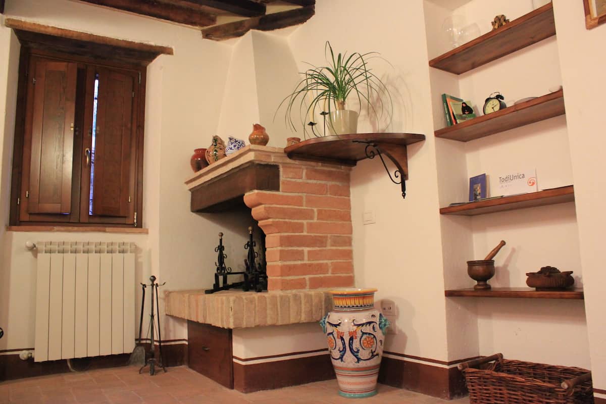 Una habitación tradicional con chimenea de ladrillo, un gran jarrón decorativo y estanterías de madera con diversos objetos.