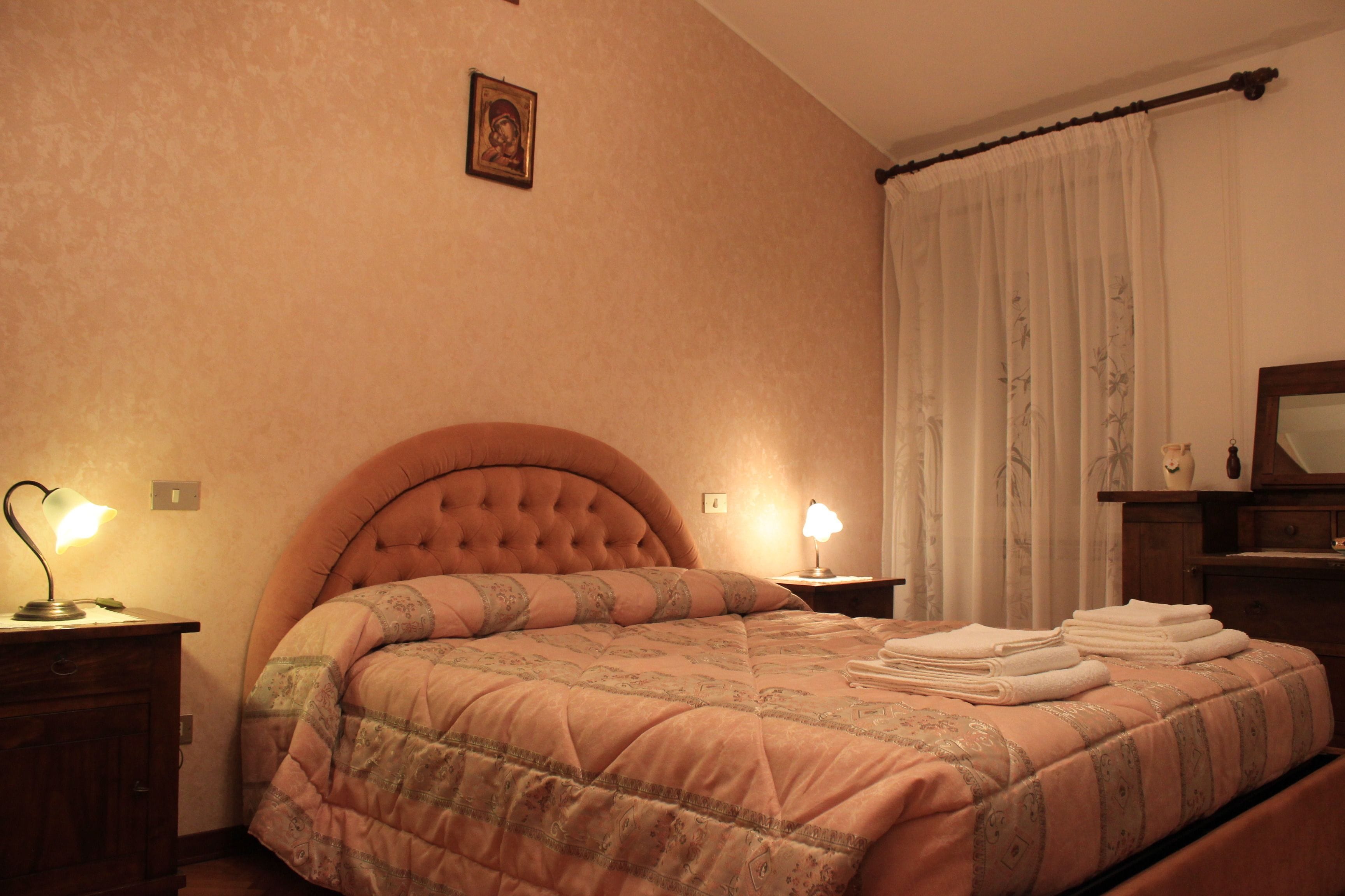 A bedroom with a large bed, two bedside lamps, a wooden nightstand, and a mirror on the wall.
