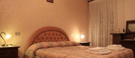 Un dormitorio con una cama grande, dos lámparas de noche, una mesita de noche de madera y un espejo en la pared.