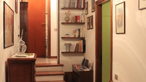 A staircase leading to a second floor, a wooden bench with floral upholstery, a bookshelf with various books, and a hanging light fixture. - Il Focolare (Todi)