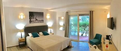 A hotel room with a bed, bedside lamps, a desk with a chair, a television, and a large window with a view of greenery.