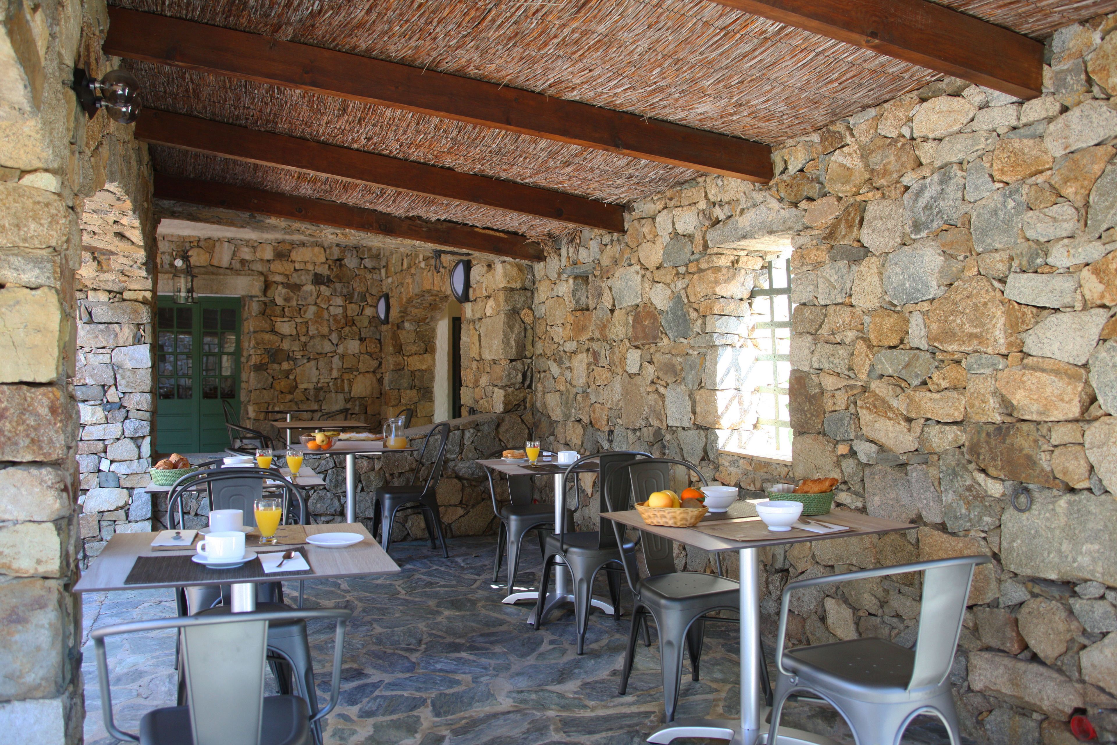 A stone-walled dining area with tables and chairs, breakfast items, and a rustic ceiling.