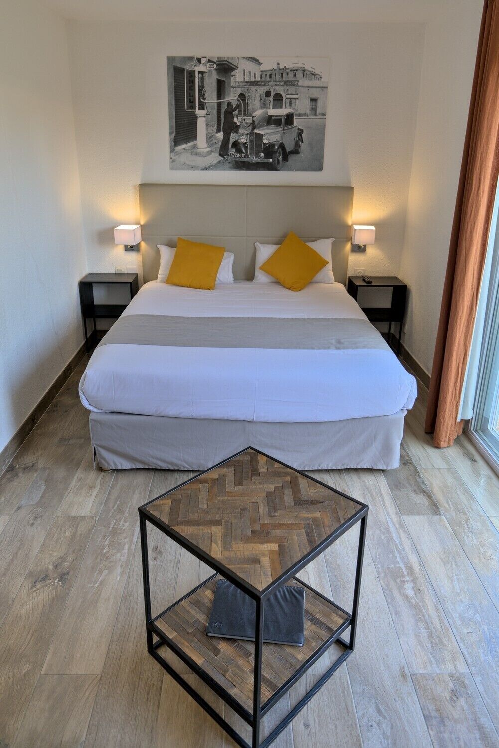 A hotel room with a large bed, two bedside tables, a small wooden table, and a picture on the wall.