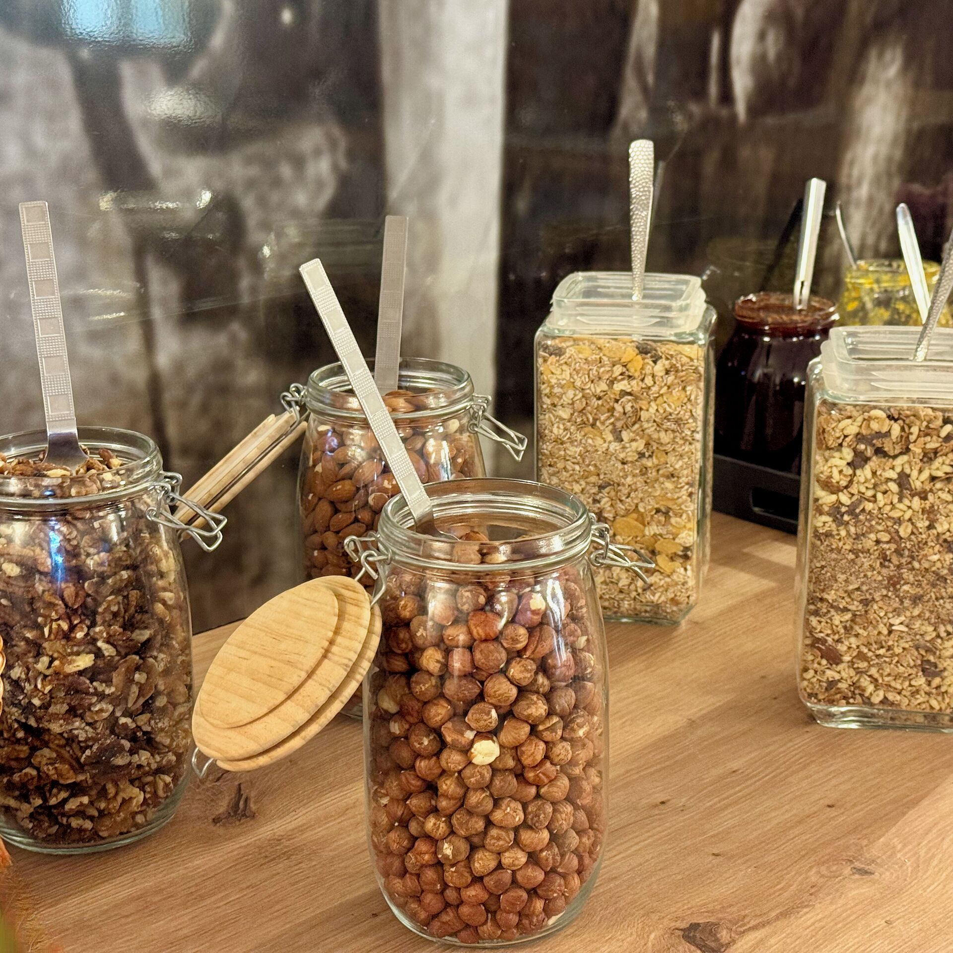 A variety of food items in glass jars with metal lids and straws, displayed on a wooden surface.