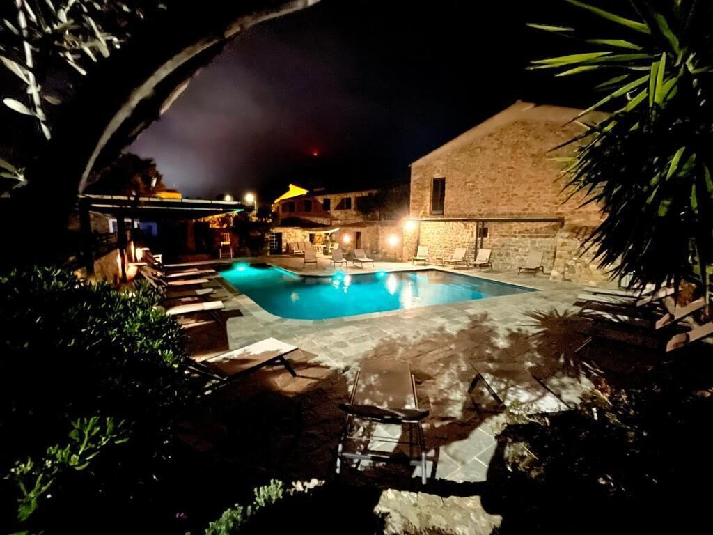 A nighttime swimming pool area with lounge chairs and a stone building.