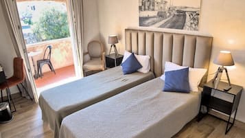 A room with two beds, a window, a chair, a table, and a lamp.